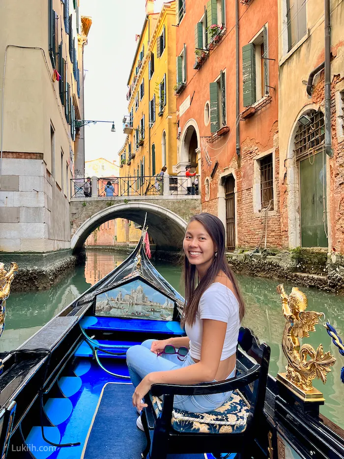 A woman sitting on a boat floating on a small canal surrounded by colorful buildings.