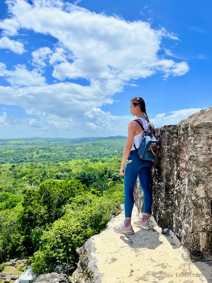 A woman standing at the ledge of a structure overlooking a lush rainforest.