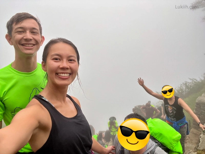 A selfie of four people standing on a mountain with fog blocking the view behind them.