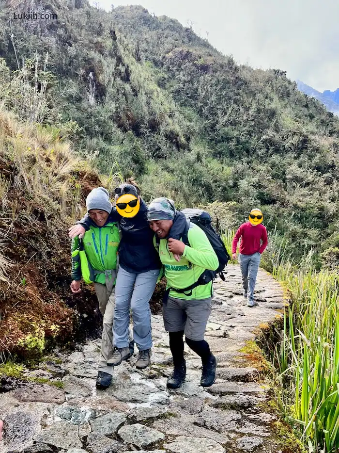 Two men carrying a woman around their shoulders on a mountain trail.
