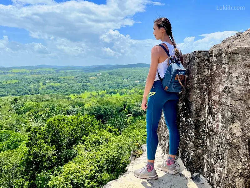 A woman standing at the ledge of a structure overlooking a lush rainforest.