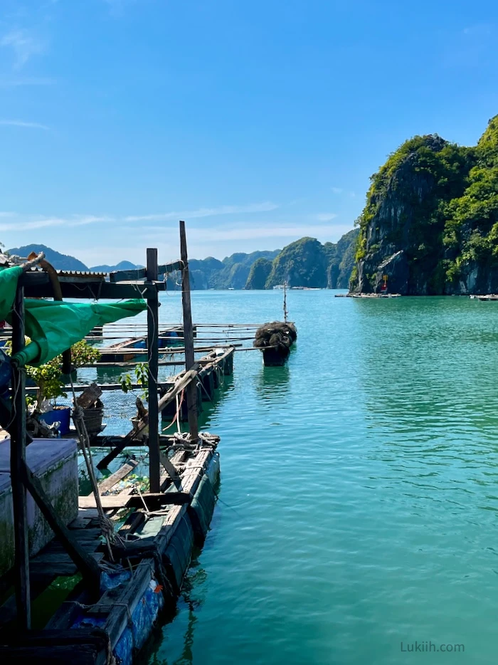 Wooden makeshift boats floating over emerald water with limestone karsts in the landscape.