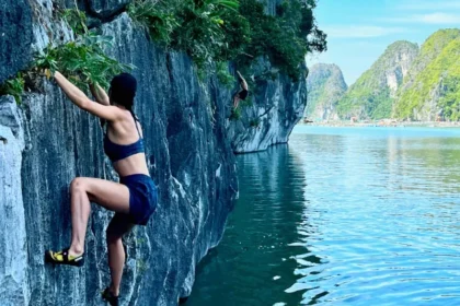 A closeup of a woman climbing up a gray limestone rock over water without any ropes.