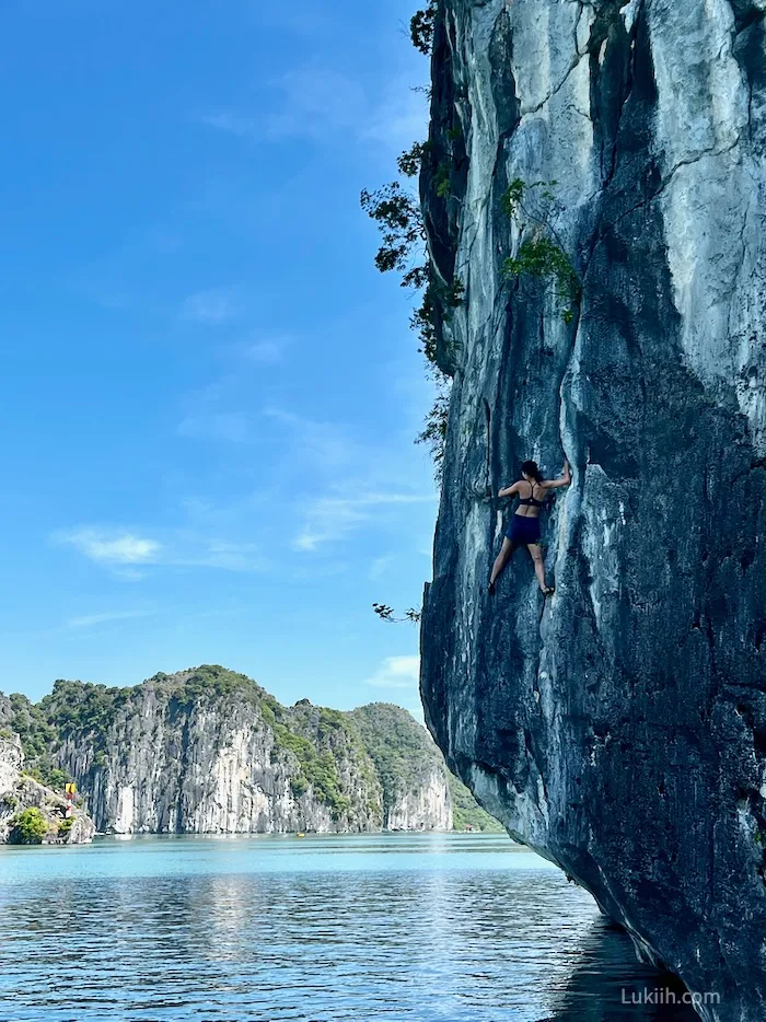 A woman climbing up a gray limestone rock over water without any ropes.