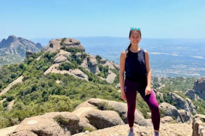A woman in athletic clothing standing on a mountain with sky blue views in the horizon.