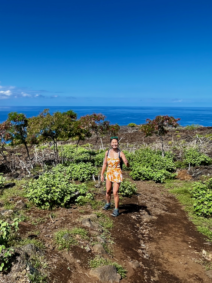 A woman hiking on dirt path with no shade overlooking the ocean.