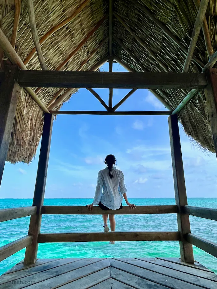 A woman sitting on a beam looking out at a very clear and blue ocean.