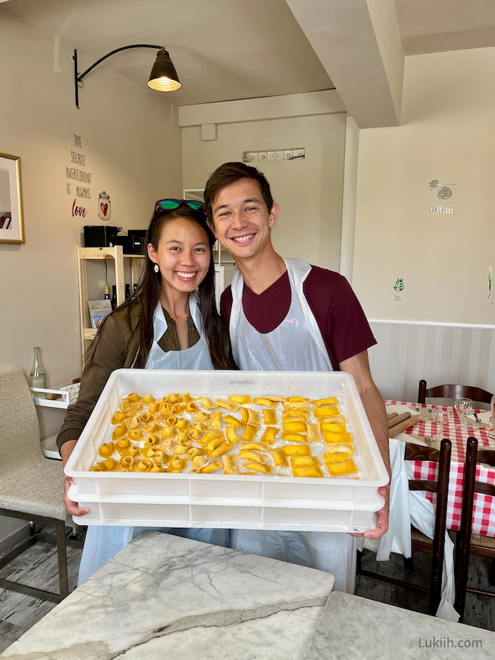 Two people holding a container with freshly-made pasta.