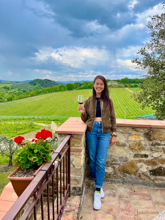 A woman holding a glass of red wine against a field of grapes.