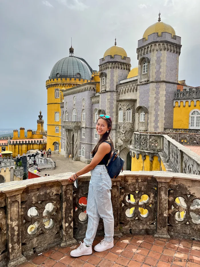 A woman standing in front of a historic yellow and purple castle.