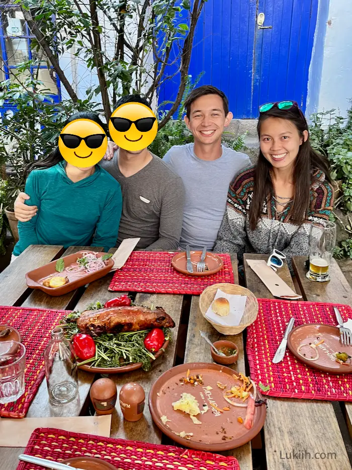 Four people about to eat a dish holding a whole roasted guinea pig.