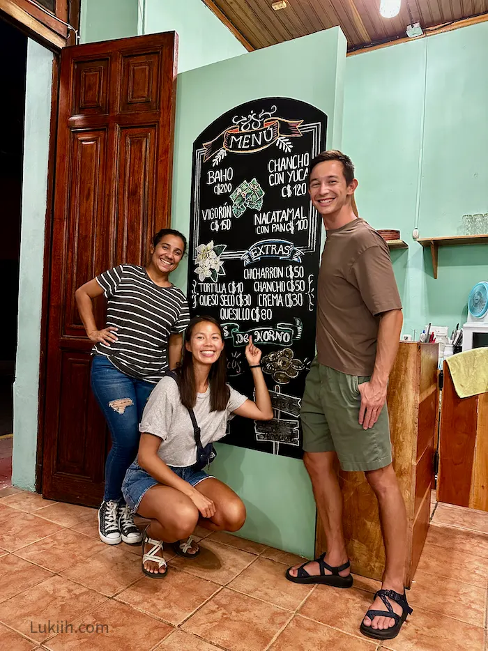 Three people standing next to a menu with typical Nicaraguan food on it.