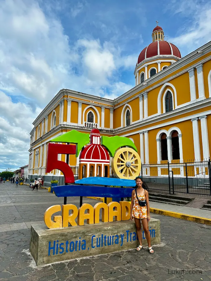 A woman standing next to a Granada sign with a yellow church in the background.