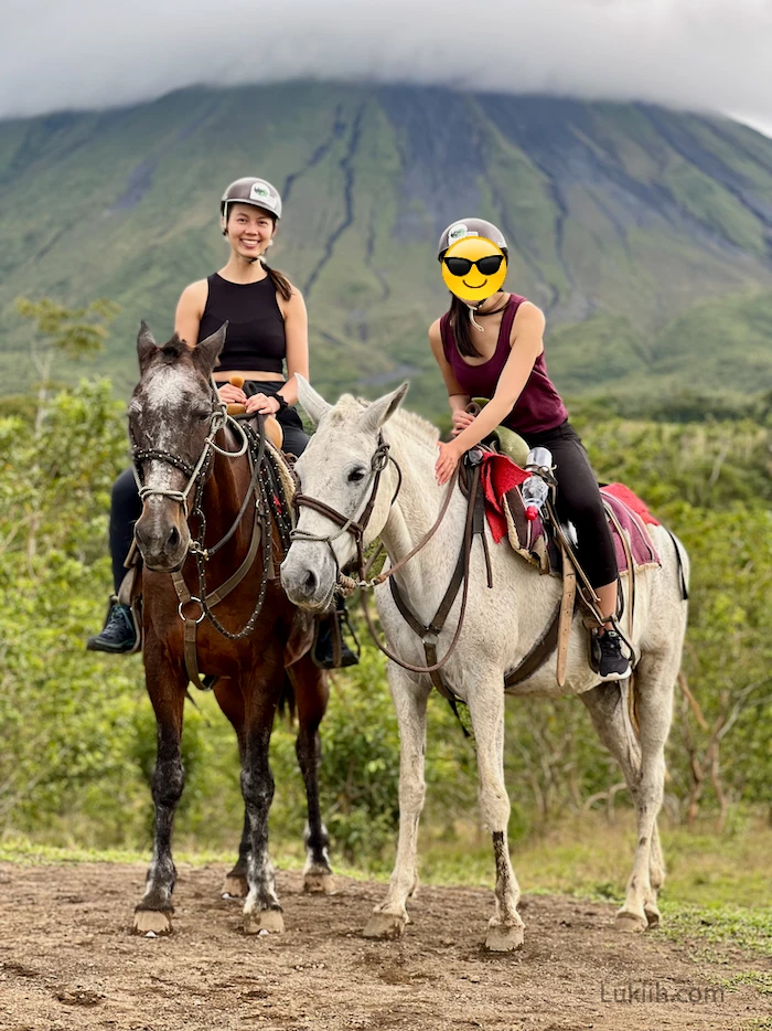 Two people riding horses with a volcano in the background.