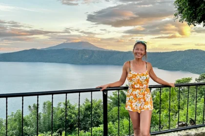 A woman standing at a viewpoint with a volcano and a lake in the background.