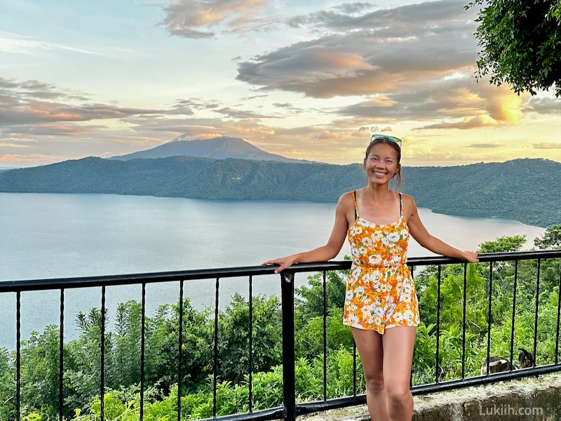 A woman standing at a viewpoint with a volcano and a lake in the background.