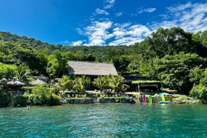 A tropical building surrounded by lush trees near a blue lake.