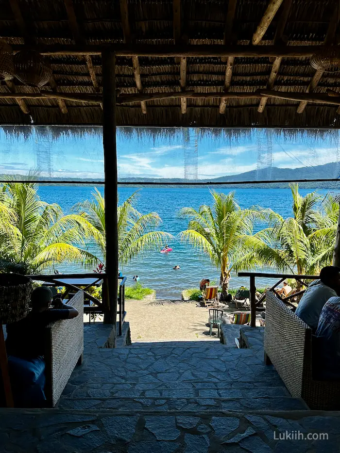 A view of a blue lake from a shaded open-air restaurant.