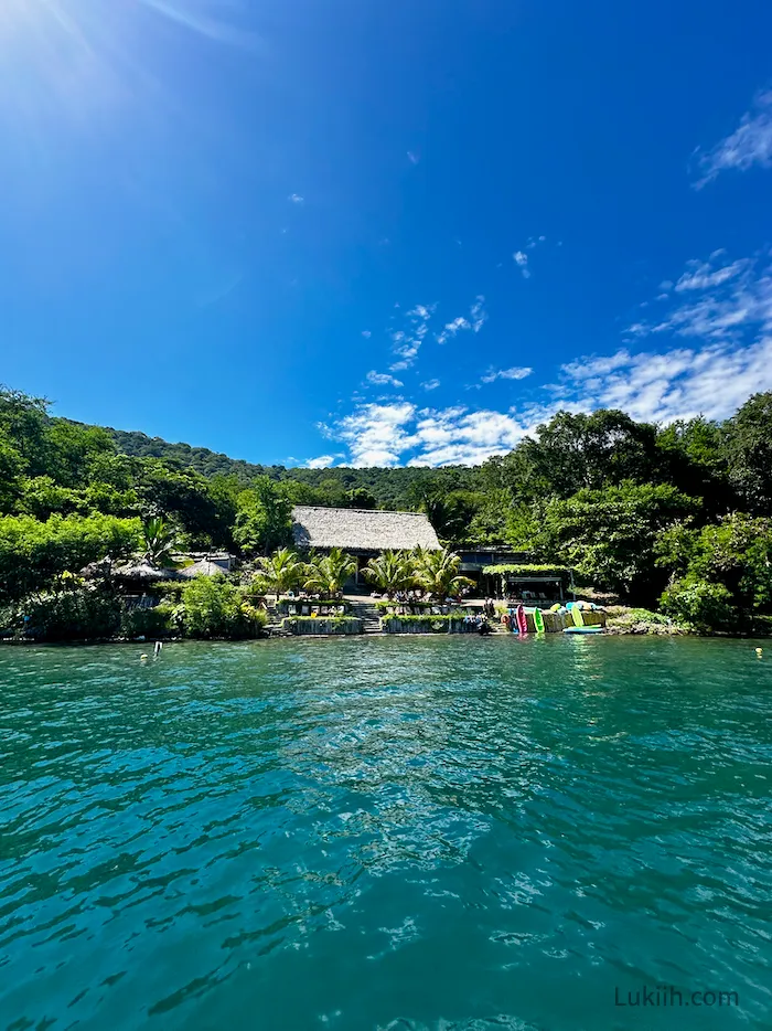 A blue lake with an open building with plants surrounding it.