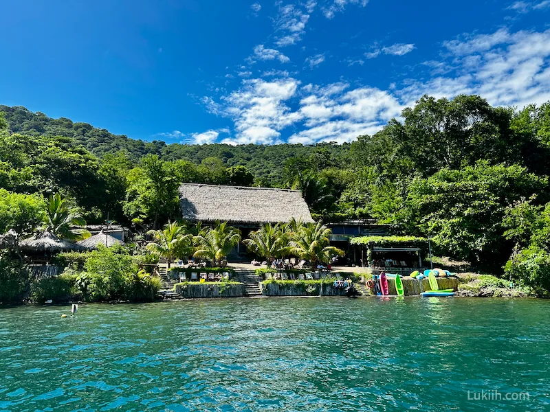 A tropical building surrounded by lush trees near a blue lake.