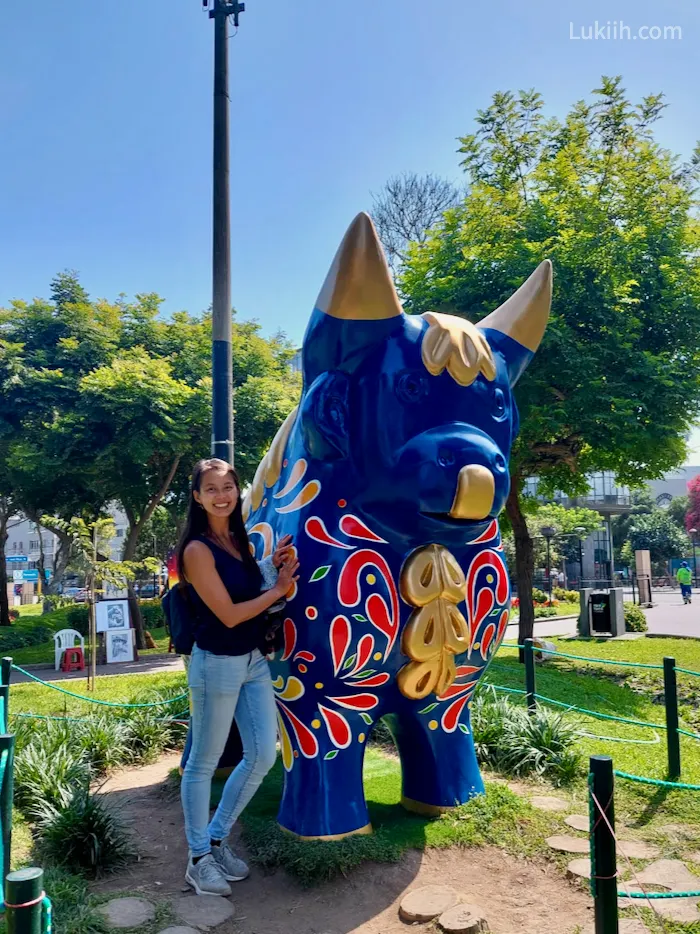 A woman standing in a park next to a bit statue of a bull