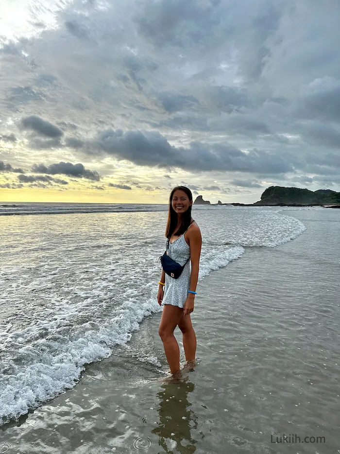 A woman standing on an empty beach with a sunset in the background.