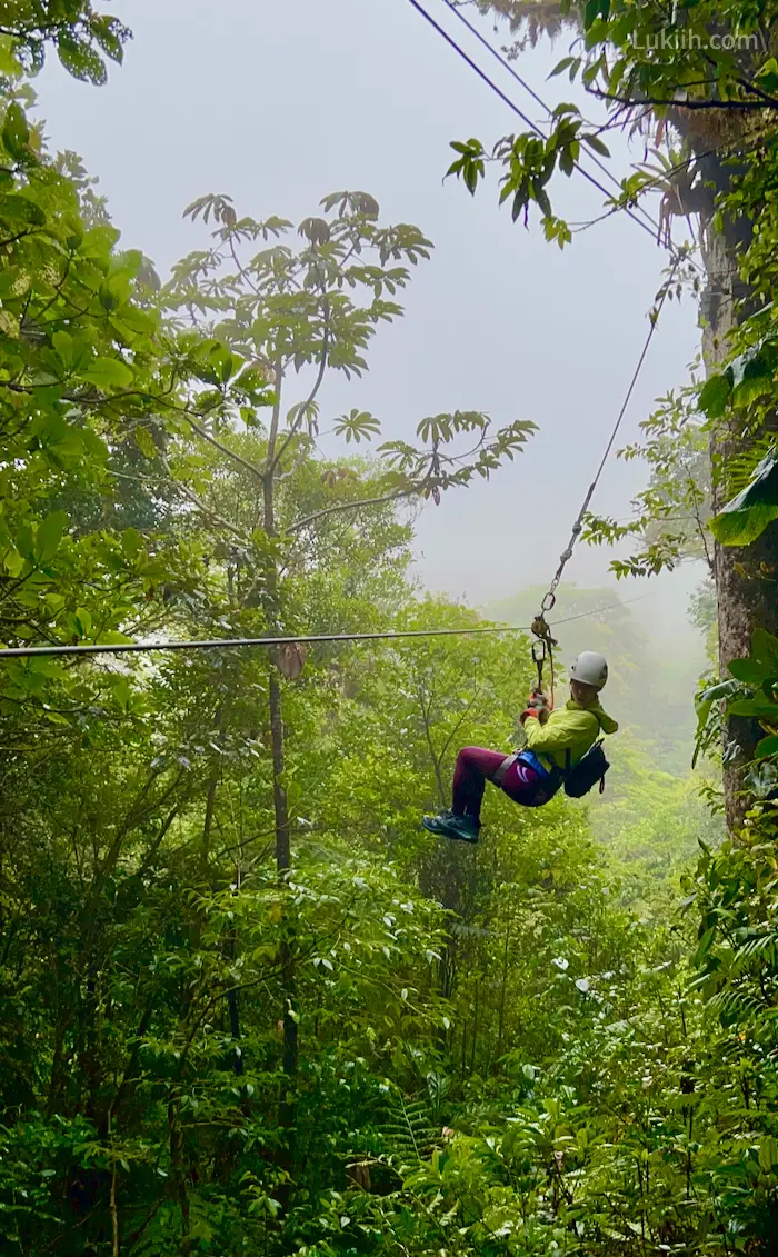 A woman hanging on a zipline overlooking a misty rainforest.