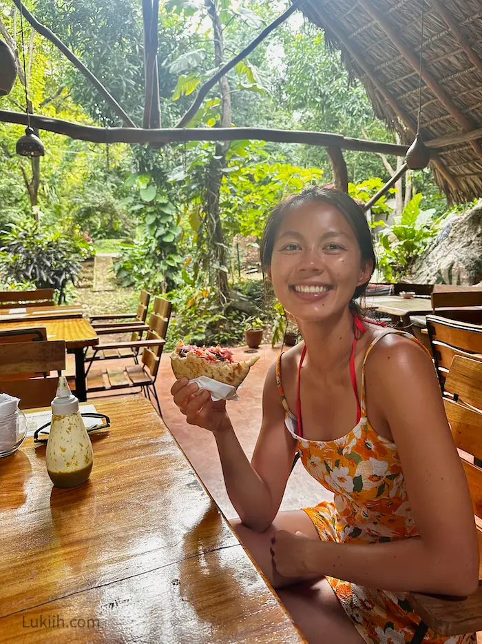 A woman holding a pita in an open-air restaurant surrounded by plants.