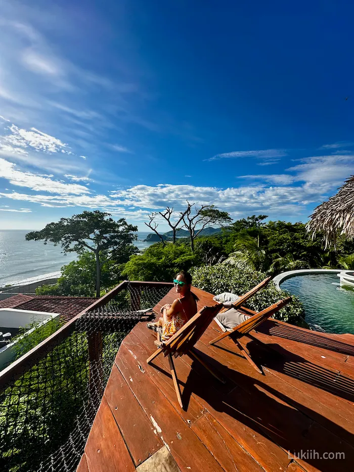 A woman sitting on a terrance overlooking the ocean.