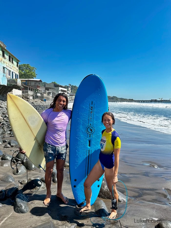 Two people standing on a rocky beach with surfboards.