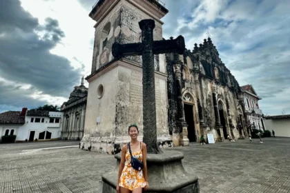 A woman standing in front of a large cross in front of an ornate church.