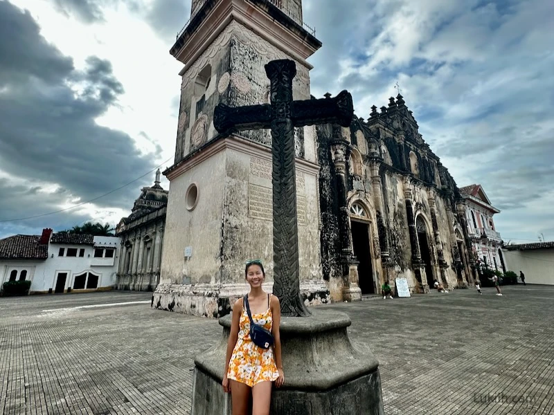 A woman standing in front of a large cross in front of an ornate church.