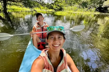 Two people kayaking over water surrounded by lush trees.