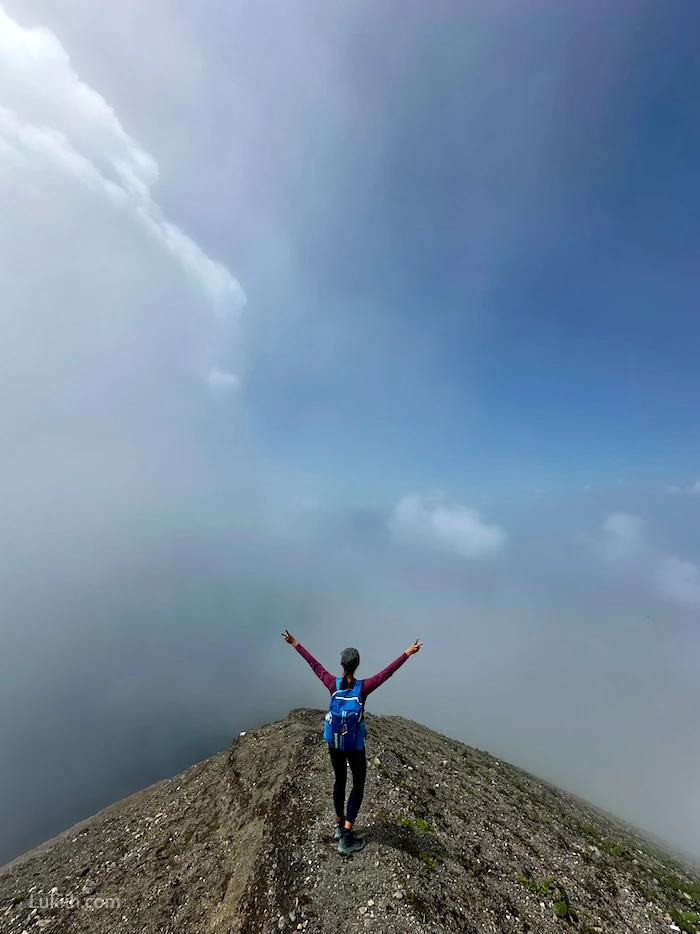 A hiker at the top of a mountain, but the view is obscured by clouds.