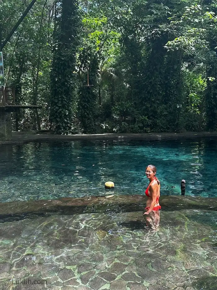 A woman inside a crystal-clear pool surrounded by trees.