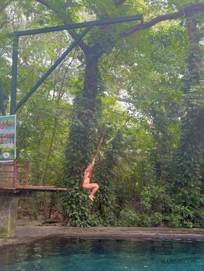 A woman swinging off a rope into a crystal-clear pool.