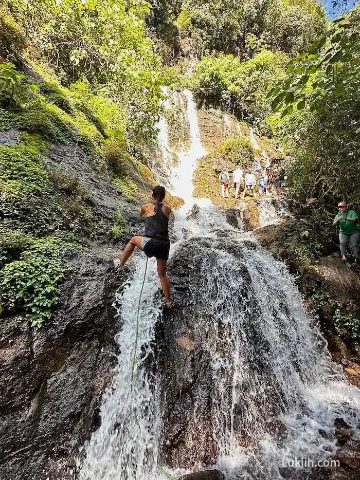 A woman holding onto a rope while climbing up a waterfall.