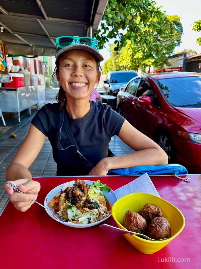 A woman sitting outside on the street with a plate of yucca and nuegados.