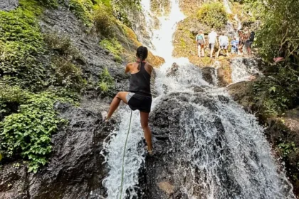 A woman holding onto a rope while climbing up a waterfall.