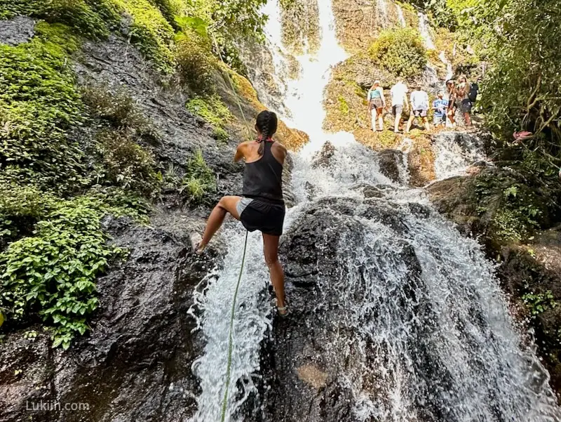 A woman holding onto a rope while climbing up a waterfall.