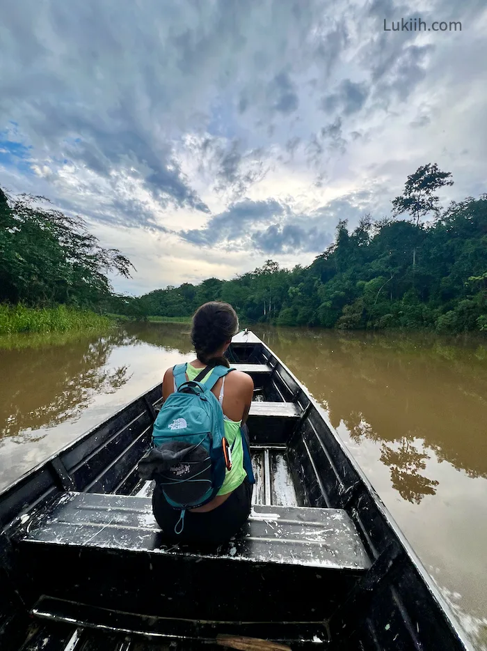 A woman sitting on a small boat on a river with lush rainforest.