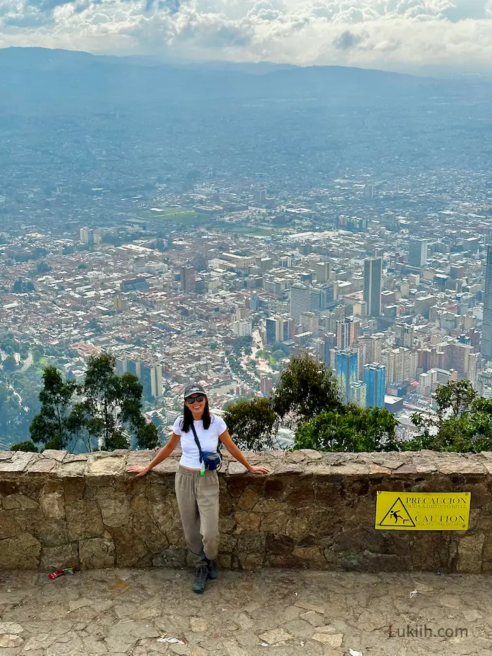 A woman standing next to a ledge with a vast city background behind.