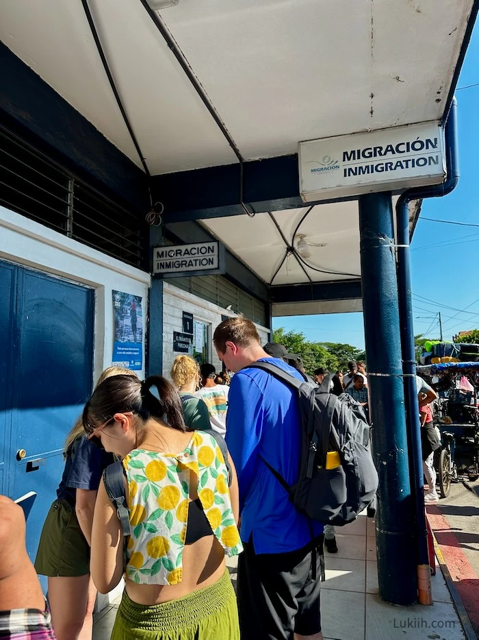 Multiple people waiting in line under a sign that says MIGRACION/INMIGRATION