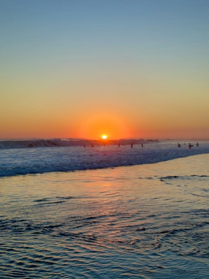 Sunset over a beach area with many surfers