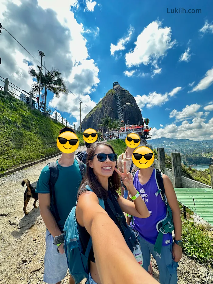 A woman taking a group selfie with a giant rock protruding out in the background.