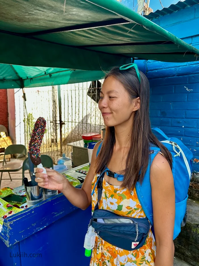 A woman holding a frozen banana covered in chocolate.