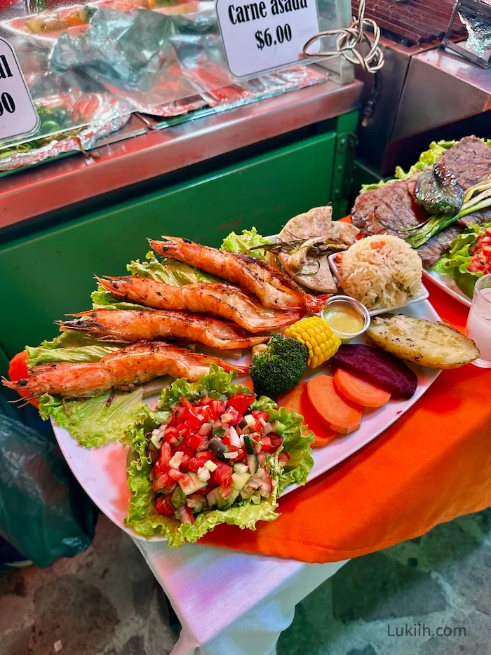 A platter with shrimp, carrots and salad.