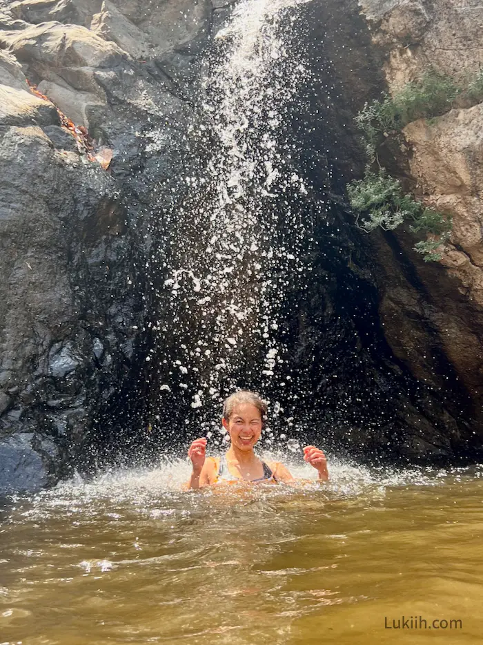 A woman smiling under a small waterfall.