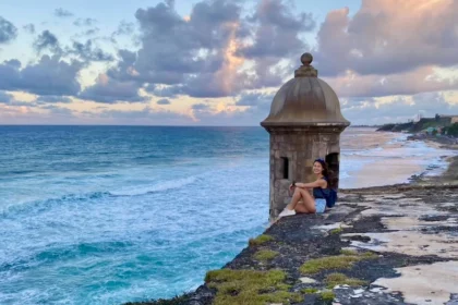 A woman sitting on a ledge next to a clear blue ocean.