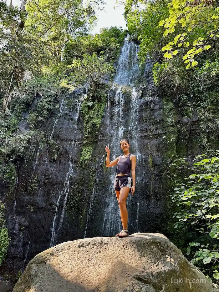 A woman standing on a rock with a waterfall in the background.